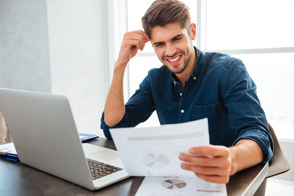 Young cheerful man sitting at home while looking on paper offshore private wealth management